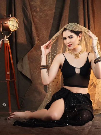 A playful, barefoot pose in a modern fusion look. The studio setting with rustic props adds character and context to this creative Indo-western fashion shot.