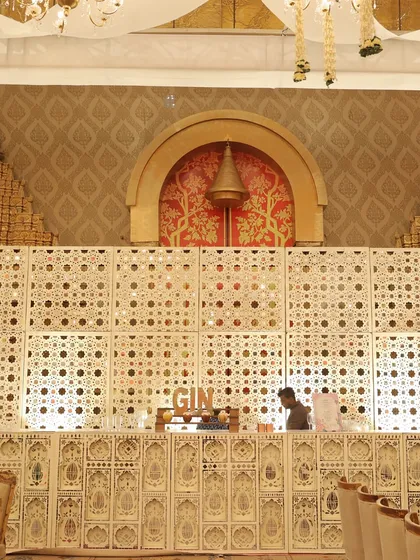 An ornate bar setup, featuring a custom-built facade with intricate jaali work, seamlessly integrated into the golden wedding theme.