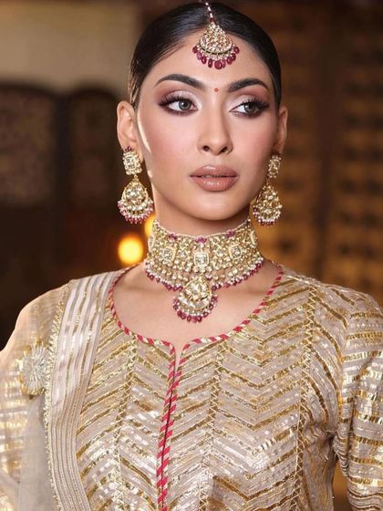 A close-up of a timeless bridal look. The makeup features a classic winged liner and a soft, neutral lip, paired with a traditional gold and ruby maang tikka.