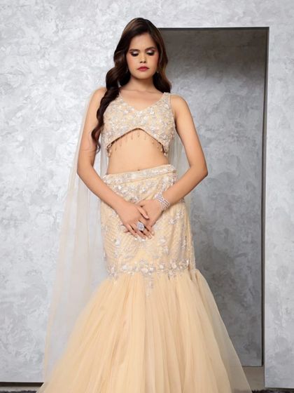 A professional shot of a model in a beige mermaid-style lehenga-gown with a delicate cape. This silhouette is perfect for a cocktail or engagement party.