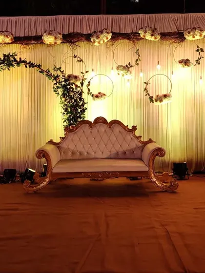 A wider view of the rustic glam stage, showing the full setup on the carpeted platform. The warm uplighting on the curtain backdrop adds depth and highlights the intricate floral and branch details.