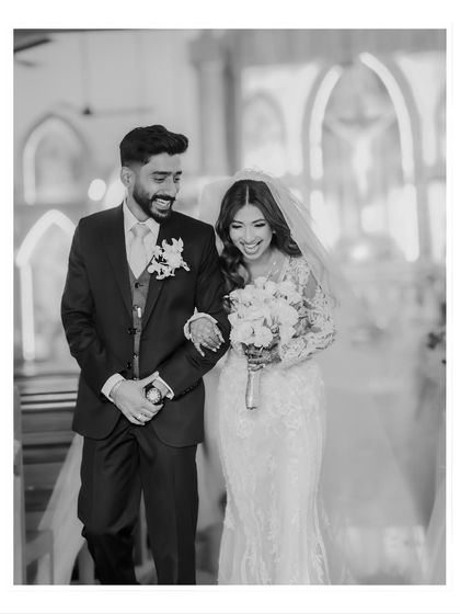 A joyful black and white candid of the couple walking down the aisle after their ceremony. The monochrome format highlights their happiness and the church's architecture.