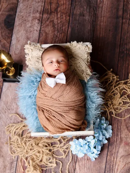 A dapper little gentleman! This newborn looks sharp with a tiny white bowtie complementing his brown swaddle, set against a rustic backdrop with blue and brown accents.