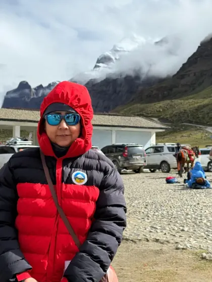 A pilgrim stands ready, bundled against the cold, with the mystical peak of Kailash shrouded in clouds behind her.
