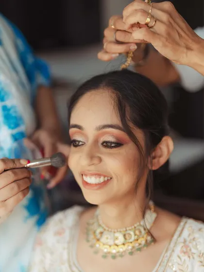 The bride's happy smile as the makeup artist applies the finishing touches.