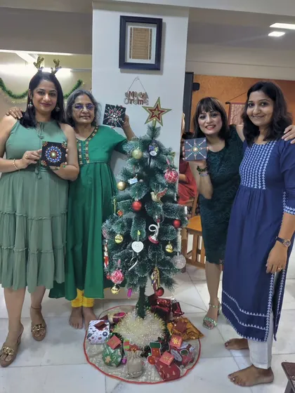 Friends gather around a Christmas tree, holding up the dot mandala art they created during a festive holiday party.