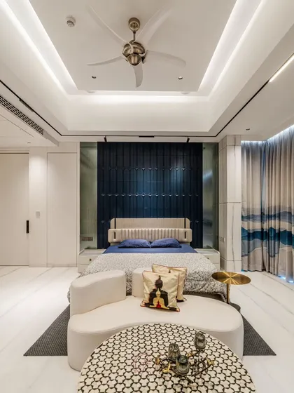 This master bedroom features a striking navy blue 3D paneled accent wall, creating a sense of depth and drama. The custom curved sofa and patterned coffee table add a layer of bespoke elegance to the space.
