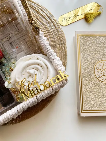 An elegant Eid gift basket featuring a rolled prayer mat, a mini Quran, and an acrylic "Eid Mubarak" sign.