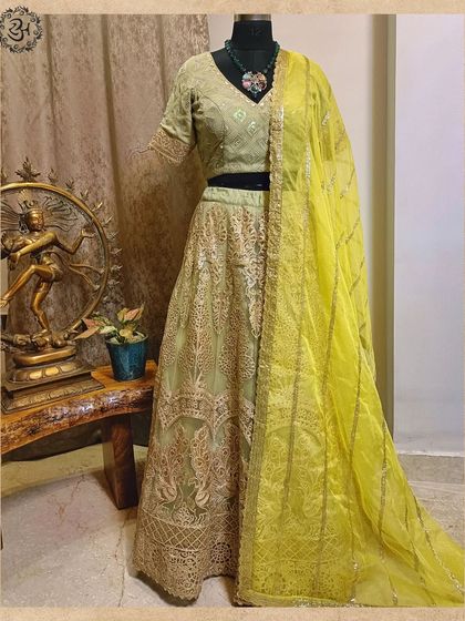 This gorgeous green lehenga is perfect for the wedding season. The net skirt is layered with delicate embroidery, and the matching blouse is paired with a contrasting bright yellow dupatta for a fresh, festive look.