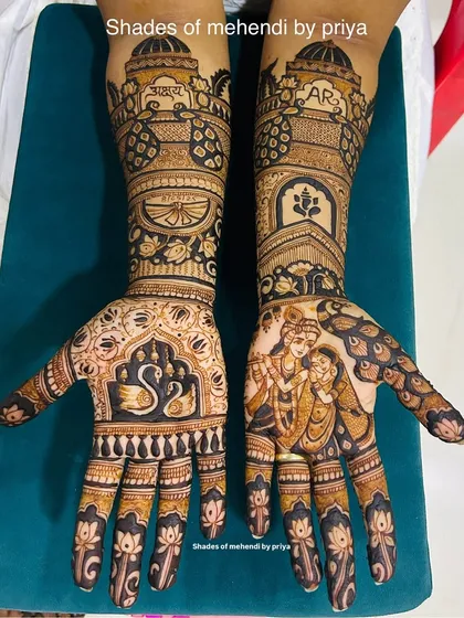 A full bridal mehendi set that showcases a mix of styles. One hand features a beautiful Radha-Krishna figure, while the other has elegant swan motifs and the couple's initials. The arms are decorated with traditional architectural and floral patterns.
