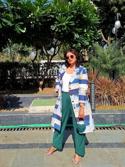 A sustainable fashion choice with this trench coat made from upcycled materials. Paired with green trousers and a heart-shaped bag, it's a quirky and conscious look.