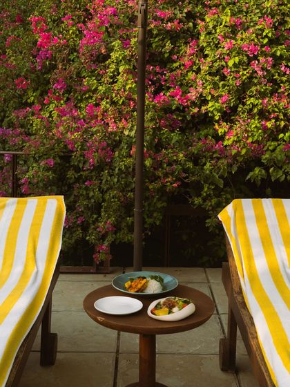 A poolside meal set between two loungers, against a vibrant wall of pink bougainvillea.