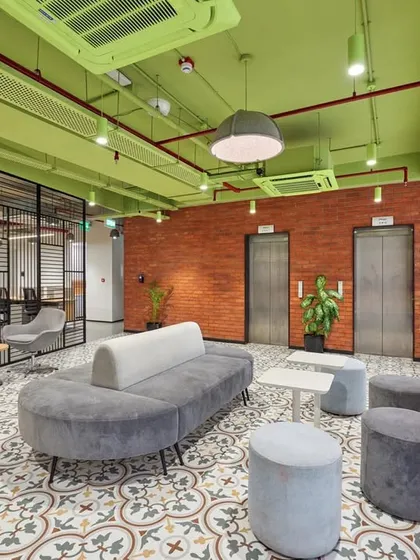 A lift lobby lounge with a vibrant green ceiling and exposed brick walls. The patterned floor tiles and comfortable grey sofas create a stylish waiting area.