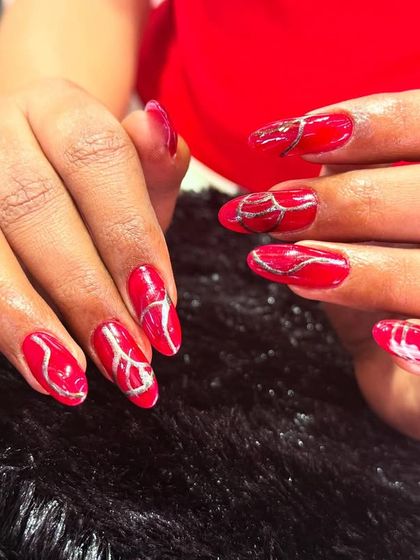 A bold and fiery set in a vibrant red. The abstract silver glitter lines swirl across the nails, creating a look of liquid energy.
