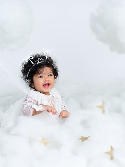 A close-up of our little angel's happy face. Her bright smile and curly hair are the stars of this heavenly cloud-themed photo.
