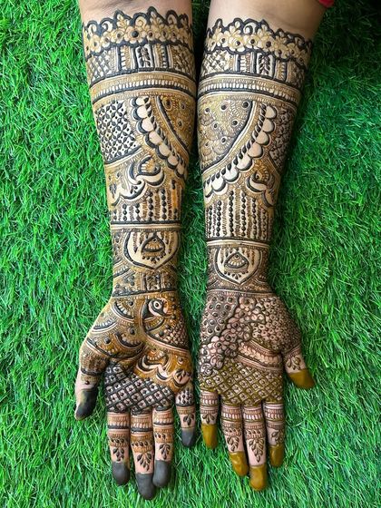 Another angle of this gorgeous full bridal mehendi, set against a vibrant green background. The contrast makes the fine lines and bold shapes of the peacock and architectural patterns pop.