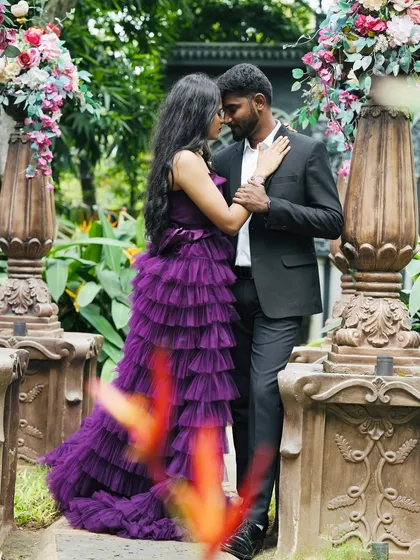 Finding the perfect couple's outfit is easy here. This purple ruffle gown for her and a classic black suit for him create a perfectly coordinated and elegant look for a pre-wedding shoot in a beautiful garden setting.