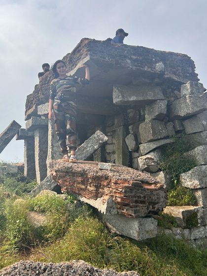 A trekker stands victoriously atop the ruins of the old fortress at the Skandagiri summit.