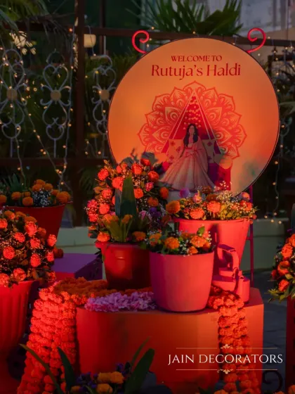 A warm and personalized welcome to the Haldi ceremony. The entrance features a custom sign with the bride's illustration, surrounded by pots of bright orange marigolds, setting a joyful and personal tone.
