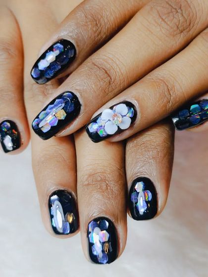 A full look at the black nails with iridescent floral glitter and a 3D flower accent, creating a beautiful, multi-dimensional effect.