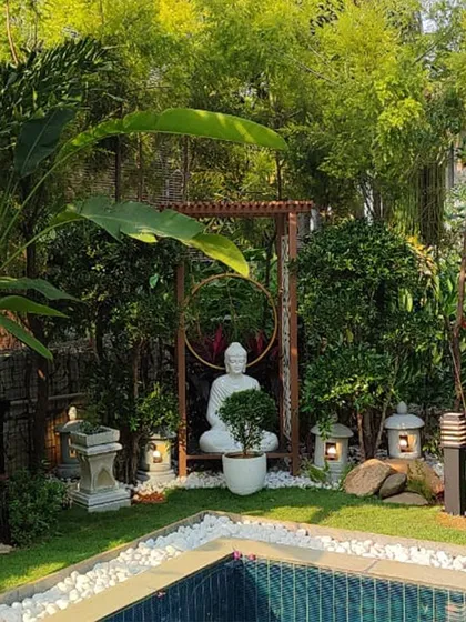A serene Buddha statue creates a point of tranquil focus in this poolside Zen garden. We carefully selected white pebbles, stone lanterns, and lush bamboo to frame the setting, designing a space for quiet contemplation that harmonizes with the water.