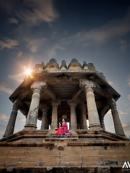 A moment of serenity within a historic temple. The dramatic sky and ancient architecture provide a stunning backdrop for our traditional pink silk saree.