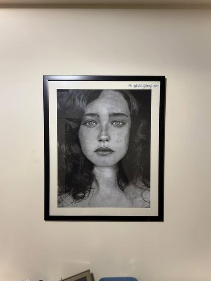My hyper-realistic charcoal portrait, framed and hanging on the wall. The simple black frame and white mount help the piece command attention.