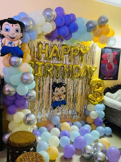A Chhota Bheem themed 3rd birthday party. The home setup includes a balloon arch with character cutouts against a silver foil curtain.