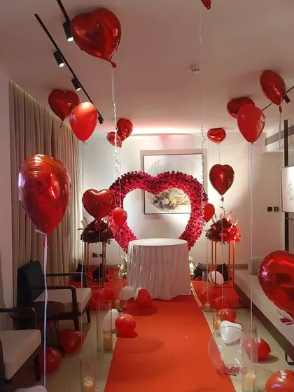 We also specialize in creating intimate and romantic birthday surprises. This setup features a red carpet aisle, a heart-shaped arch made of red roses, and dozens of red heart-shaped foil balloons to create a truly special and memorable celebration for a loved one.