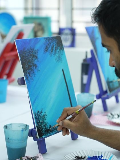 A close-up of a participant painting a night sky on canvas. The dabbing technique is used to create the effect of distant trees.