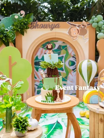 Shourya's "Wild One" safari party dessert table. This setup is packed with details, including a multi-tiered cake, animal-themed treats, and a backdrop filled with friendly lion, monkey, and giraffe figures.