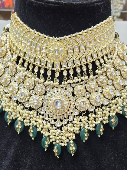 A heavy, intricate bridal choker with Kundan work and green bead drops, displayed on a bust to show its full glory.