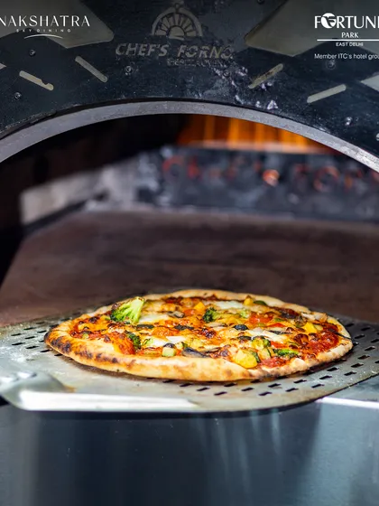 A freshly baked pizza emerging from our authentic wood-fired oven at Nakshatra. The intense heat ensures a perfectly crisp crust and melted toppings every time.