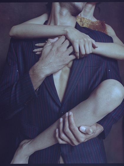 A torso shot from an archival film shoot, focusing on the embrace between two models. The styling with the pinstripe blazer and the composition create a sensual and narrative-driven image.