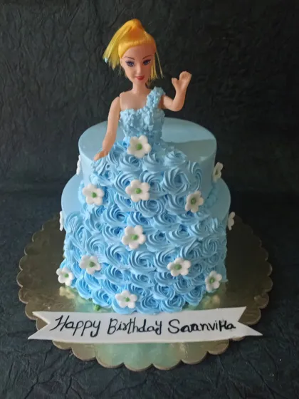 A lovely two-tiered doll cake with a blue rosette dress and delicate white flowers. It's a sweet and classic design for any little girl's birthday.