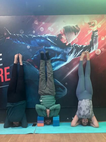 Three students demonstrate different stages of a supported headstand. We progress at our own pace, using props as needed to ensure safety and proper technique.