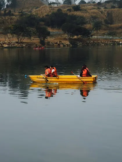 A team paddles together in a yellow boat on the calm lake, with the reflection of the sky on the water.
