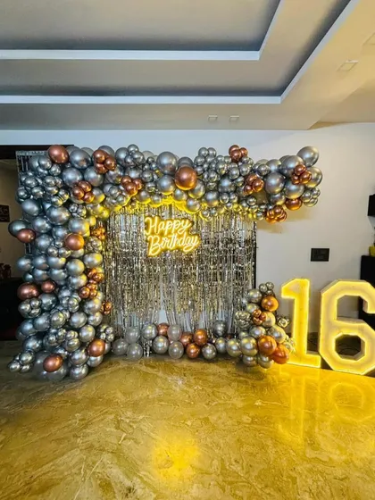 A stylish and modern 16th birthday party backdrop. This design uses a trendy silver sequin wall, a neon 'Happy Birthday' sign, and a balloon frame in metallic silver and rose gold, complemented by large light-up marquee numbers.