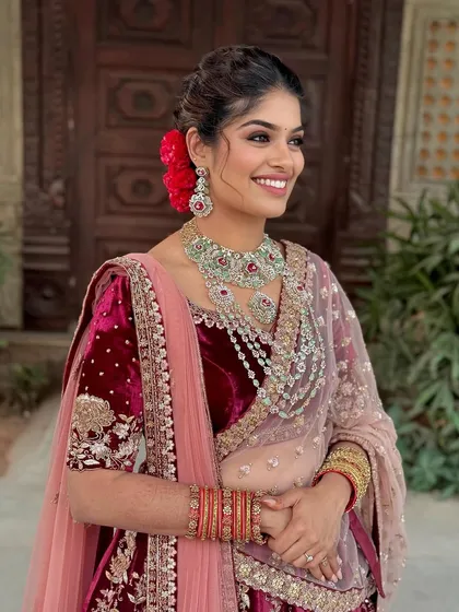 A radiant client in a maroon velvet lehenga, with kohl-rimmed eyes, glowing skin, and a modern messy updo.