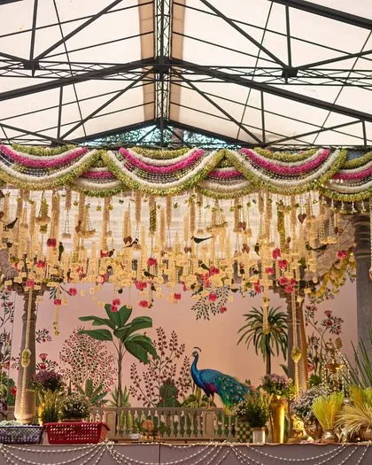 A full view of the traditional South Indian mandap, showcasing the intricate floral torans, classic temple pillars, and the beautiful hand-painted backdrop. We draped the ceiling in soft green fabric to complement the natural surroundings.