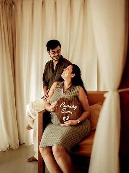 A warm indoor shot with the couple on a sofa, holding a "Coming Soon" sign. The natural light and cozy setting make for a beautiful and intimate announcement.