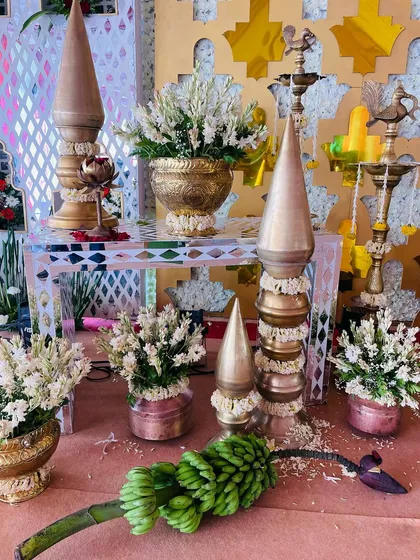 A collection of traditional props for a baby shower, including brass 'kalash' towers, banana flower buds, and white floral arrangements.