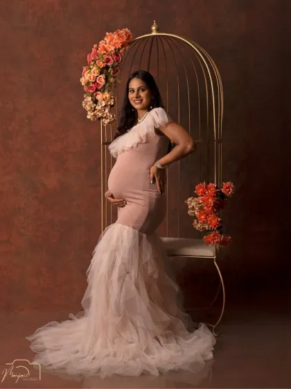 A confident and radiant pose. The combination of the flowing pink gown and the golden cage creates a stunning, high-fashion maternity look.