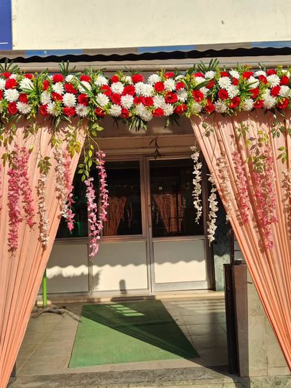 A simple and pretty entrance decoration with peach-colored drapes and a floral top piece. Perfect for house parties or small hall events.