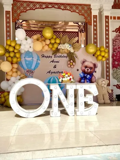 A grand teddy bear themed first birthday stage, with large 'ONE' marquee letters, a custom backdrop, and cute teddy bear props.