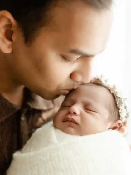 A tender close-up of a father kissing his newborn's forehead. The focus is tight on their faces, emphasizing the emotional bond.