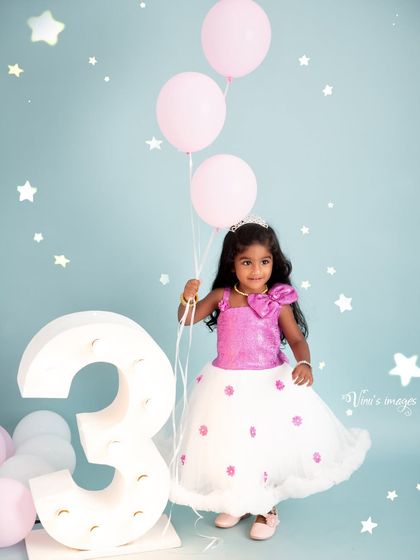 Three years young and full of charm. The birthday girl holds her balloons next to a large number three prop in this delightful studio milestone portrait.