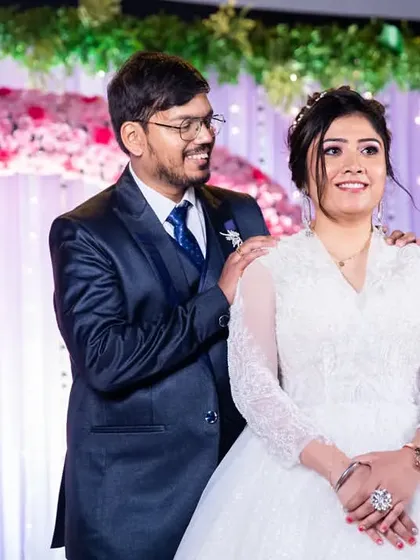 A sweet moment on the reception stage, with the groom's hands on the bride's shoulders, both looking out at their guests.