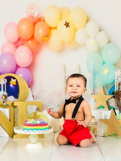 A colorful rainbow-themed cake smash to celebrate turning one! The baby boy looks delighted with his multi-colored cake.