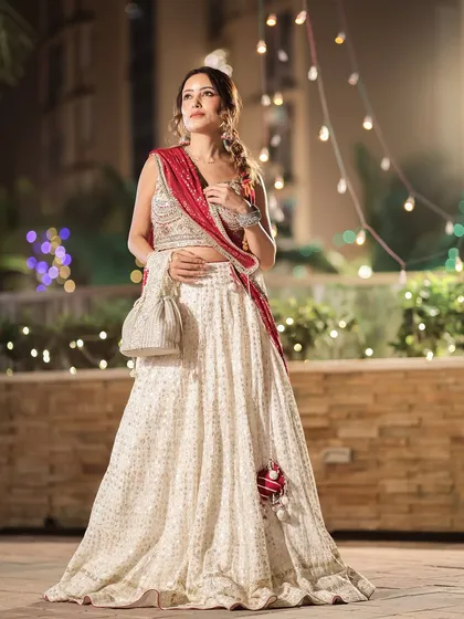 An elegant client showcases a beautiful ivory lehenga paired with a red dupatta and a stunning handcrafted potli. The accessories truly complete this festive look.